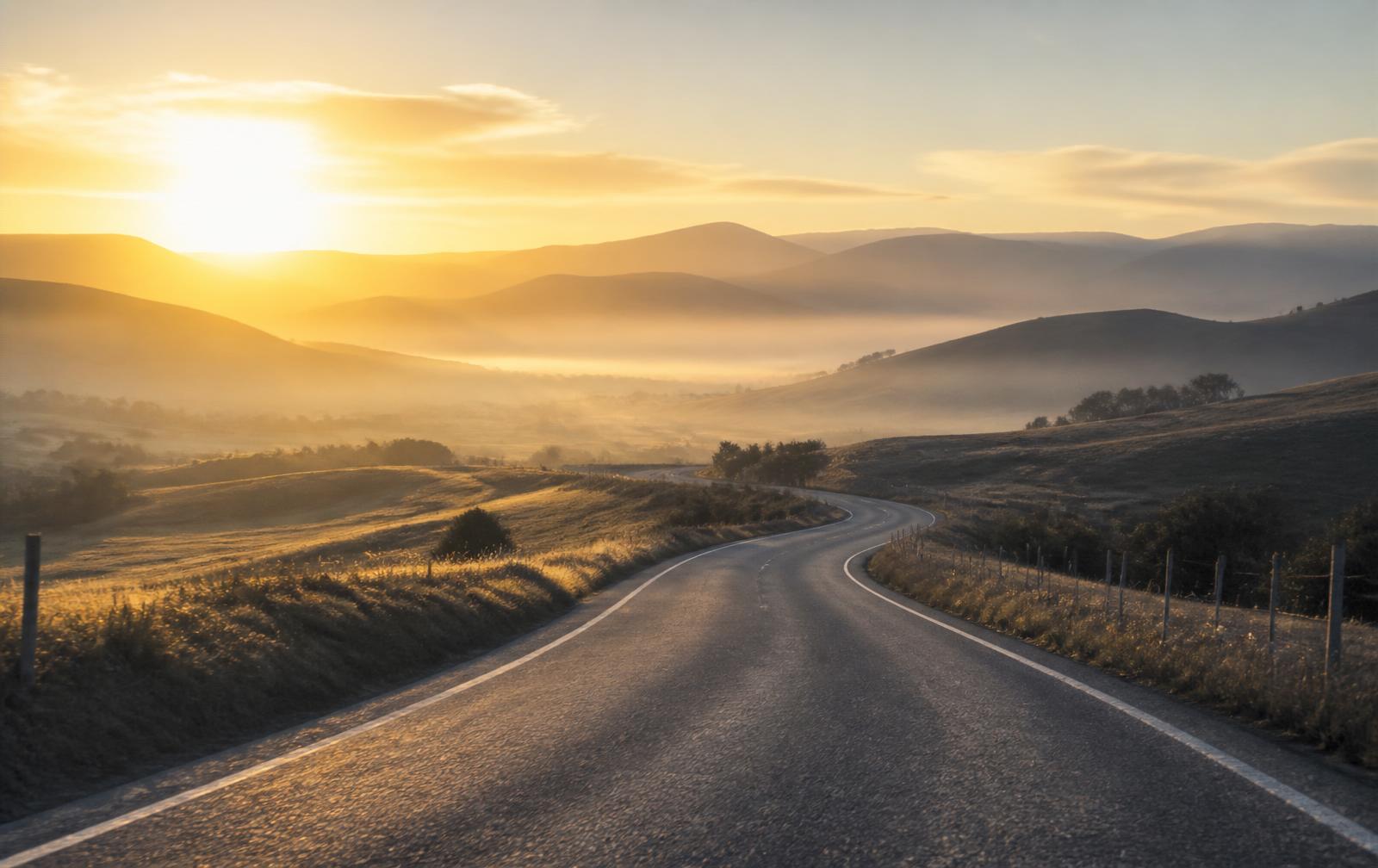 A winding road leading toward sunlit hills at sunrise